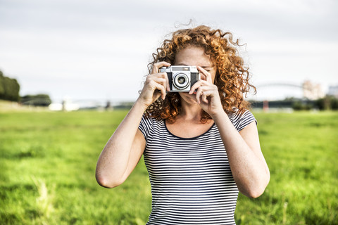 Junge Frau auf einer Wiese, die einen Betrachter mit einer Kamera fotografiert, lizenzfreies Stockfoto