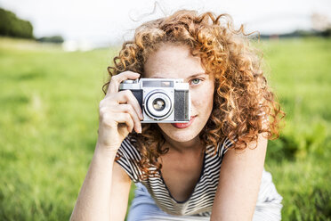 Young woman on a meadow taking picture of viewer with camera - FMKF04467