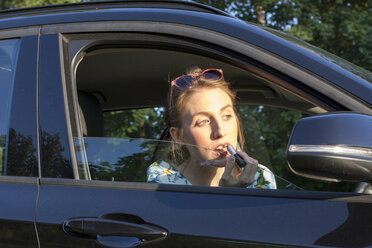 Young woman sitting in car, applying lipstick - LMF00772
