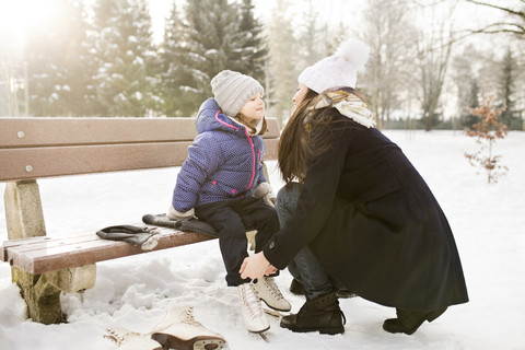 Mother helping daughter to put on her ice skates stock photo