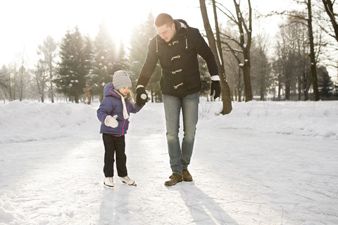 Vater und Tochter beim Schlittschuhlaufen auf einem zugefrorenen See, lizenzfreies Stockfoto