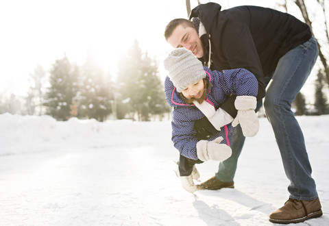 Vater und Tochter beim Schlittschuhlaufen auf einem zugefrorenen See, lizenzfreies Stockfoto