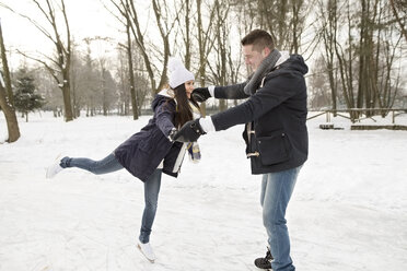 Couple ice skating on a frozen lake, woman balancing on one leg - HAPF02117