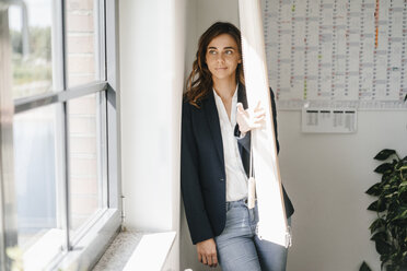 Woman standing in office, looking out of window - KNSF02713