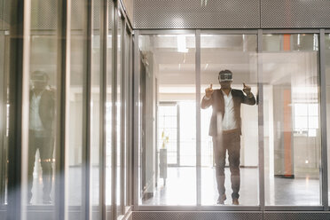 Geschäftsmann steht in einem Bürogebäude und schaut durch eine VR-Brille - KNSF02716