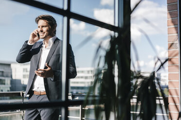 Businessman making a phone call, standing on balcony - KNSF02719