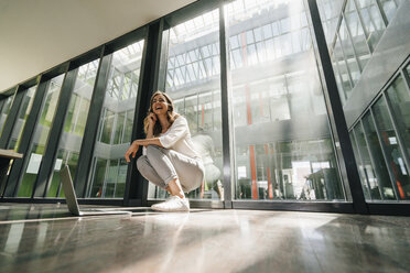 Happy businesswoman crouching on floor - KNSF02729