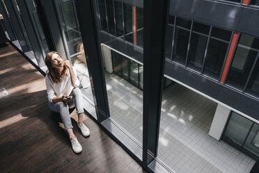 Businesswoman with smartphone, sitting on floor, daydreaming - KNSF02733