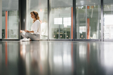Businesswoman practicing yoga in office, meditating - KNSF02735