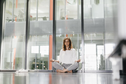 Businesswoman practicing yoga in office, meditating - KNSF02737