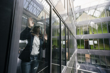 Businesswoman wearing VR goggles, standing at window - KNSF02748