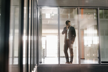 Businessman standing at window making a phone call - KNSF02768