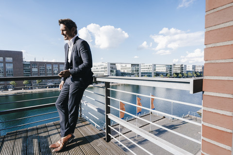 Geschäftsmann steht auf einem Balkon und hält ein Smartphone, lizenzfreies Stockfoto