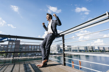 Happy businessman standing on balcony, with arms out - KNSF02776