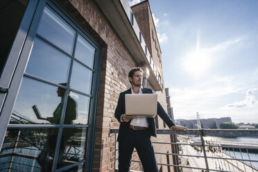 Businessman standing on balcony, using laptop - KNSF02778