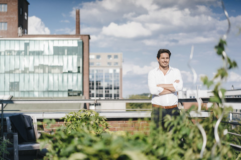 Geschäftsmann kultiviert Pflanzen in seinem städtischen Dachgarten, lizenzfreies Stockfoto