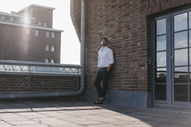 Businessman standing on rooftop terrace, with hands in pockets - KNSF02789
