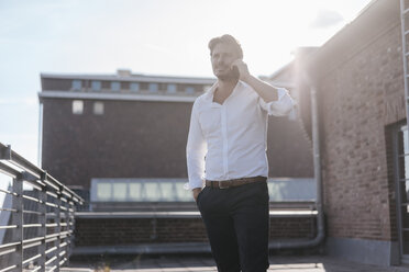 Businessman standing on rooftop terrace, making a phone call - KNSF02792