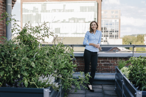 Businesswoman standing on her urban rooftop garden - KNSF02795