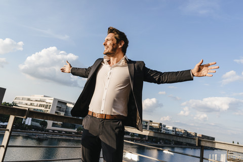 Glücklicher Geschäftsmann auf einem Balkon stehend, mit ausgebreiteten Armen, lizenzfreies Stockfoto