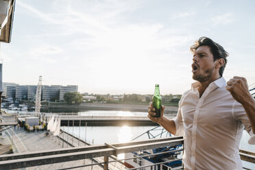 Glücklicher Geschäftsmann steht auf einem Balkon und trinkt Bier - KNSF02815