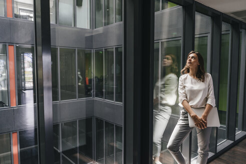 Businesswoman standing at window, holding laptop - KNSF02831