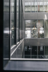 Woman standing at office window, practicing yoga - KNSF02835