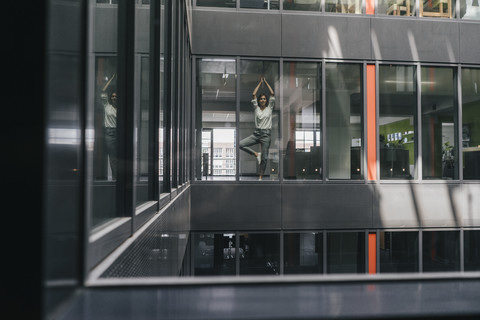 Frau steht am Bürofenster und übt Yoga, lizenzfreies Stockfoto