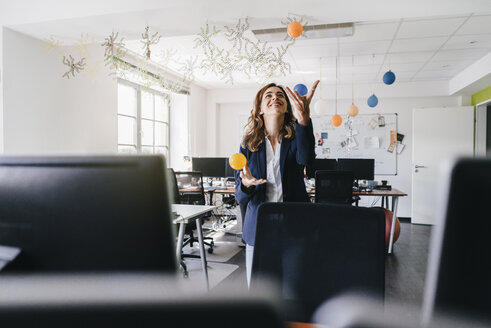 Happy businesswoman juggling balls in office - KNSF02841