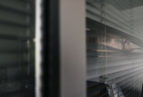 Frau steht am Fenster und späht durch die Jalousien - KNSF02852