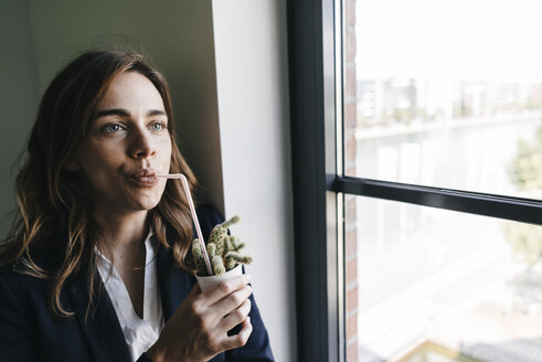 Businesswoman drinking from a straw, sticking in a cactus pot - KNSF02853