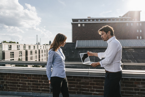 Geschäftsleute, die auf einem Balkon stehen, diskutieren und einen Laptop benutzen, lizenzfreies Stockfoto