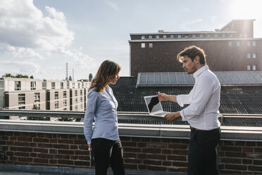 Geschäftsleute, die auf einem Balkon stehen, diskutieren und einen Laptop benutzen - KNSF02859