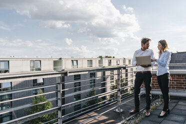 Geschäftsleute, die auf einem Balkon stehen, diskutieren und einen Laptop benutzen - KNSF02860