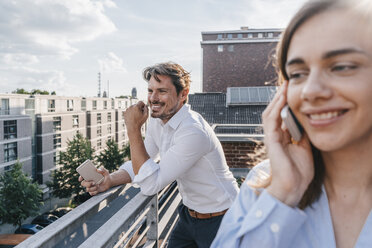 Business people standing on balcony, using smartphone - KNSF02863