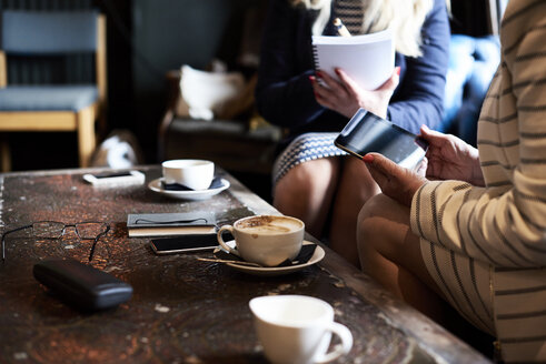 Two businesswomen with tablet and notebook having a meeting at a coffee shop - IGGF00177