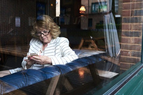 Ältere Geschäftsfrau überprüft ihr Handy in einem Café, lizenzfreies Stockfoto