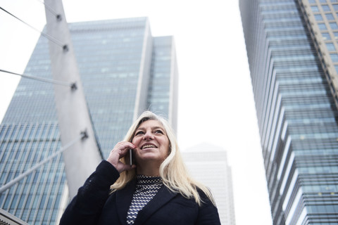 UK, London, lächelnde ältere Geschäftsfrau am Telefon in der Stadt, lizenzfreies Stockfoto