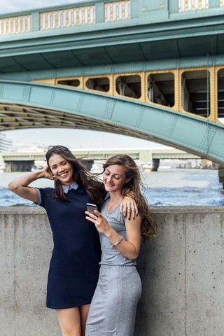 UK, London, zwei Frauen mit Smartphone am Ufer der Themse, lizenzfreies Stockfoto