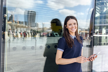 UK, London, portrait of smiling woman with smartphone in the city - MGOF03613