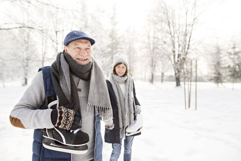 Glückliches älteres Paar mit Schlittschuhen in einer Winterlandschaft - HAPF02135