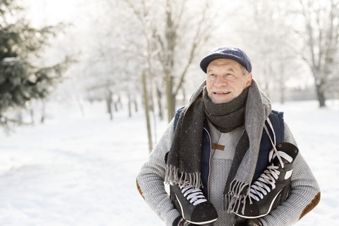 Lächelnder älterer Mann mit Schlittschuhen im Winterwald, lizenzfreies Stockfoto