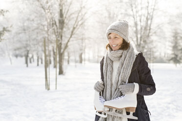 Smiling senior woman with ice skates in winter forest - HAPF02143