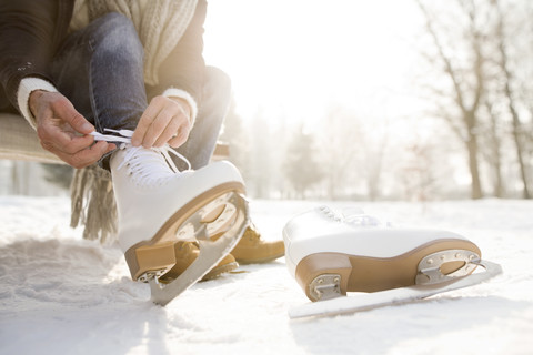 Frau sitzt auf einer Bank in einer Winterlandschaft und zieht Schlittschuhe an, lizenzfreies Stockfoto