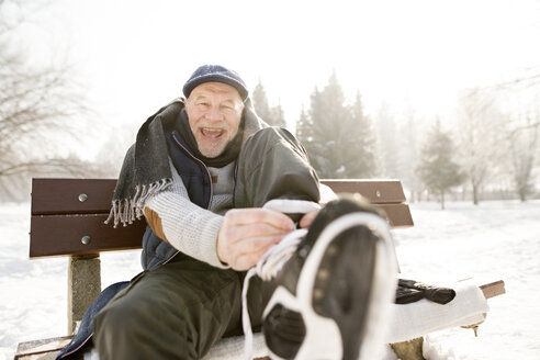 Porträt eines glücklichen älteren Mannes, der auf einer Bank in einer Winterlandschaft sitzt und Schlittschuhe anzieht - HAPF02147