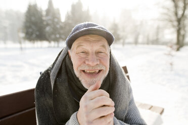 Portrait of happy senior man sitting on bench in winter landscape - HAPF02150
