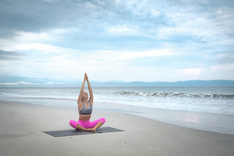 Frau übt Yoga am Strand, lizenzfreies Stockfoto