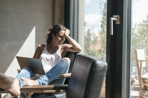 Lächelnde Frau mit Laptop entspannt sich zu Hause, lizenzfreies Stockfoto