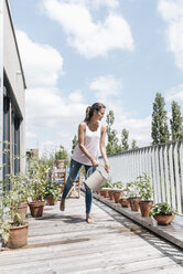 Smiling woman on balcony watering plants - JOSF01564