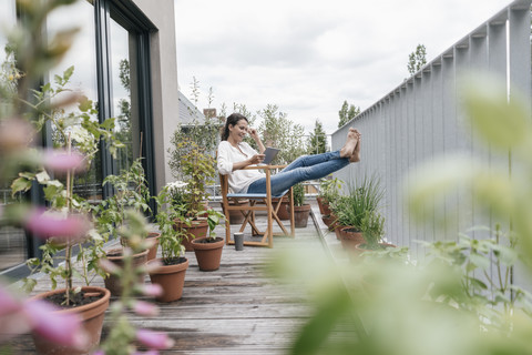 Lächelnde Frau entspannt sich auf dem Balkon und benutzt ein Tablet, lizenzfreies Stockfoto